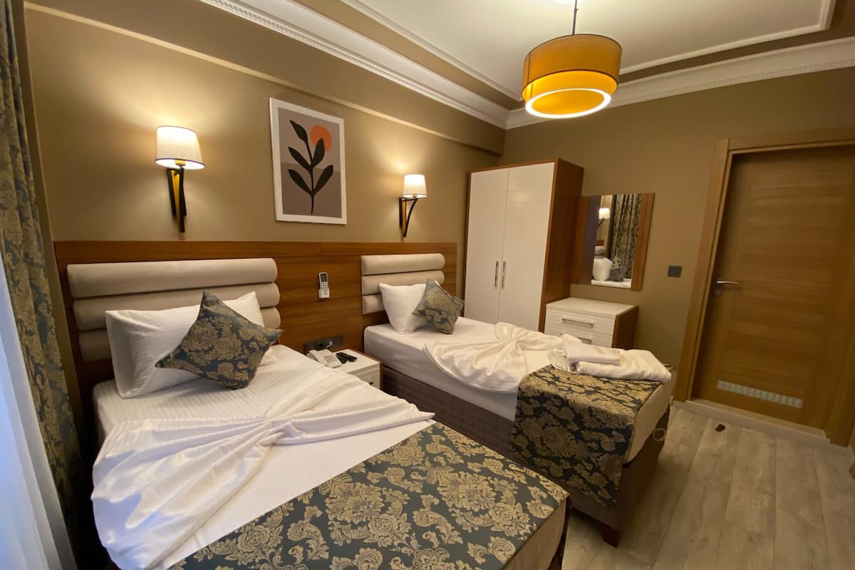Camera d'albergo con due letti, un armadio, un comodino con una lampada, uno specchio e un lampadario.