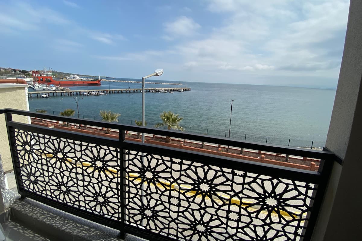 Un balcone con ringhiera decorata che si affaccia su una marina con barche e un molo che si protende nell'acqua.