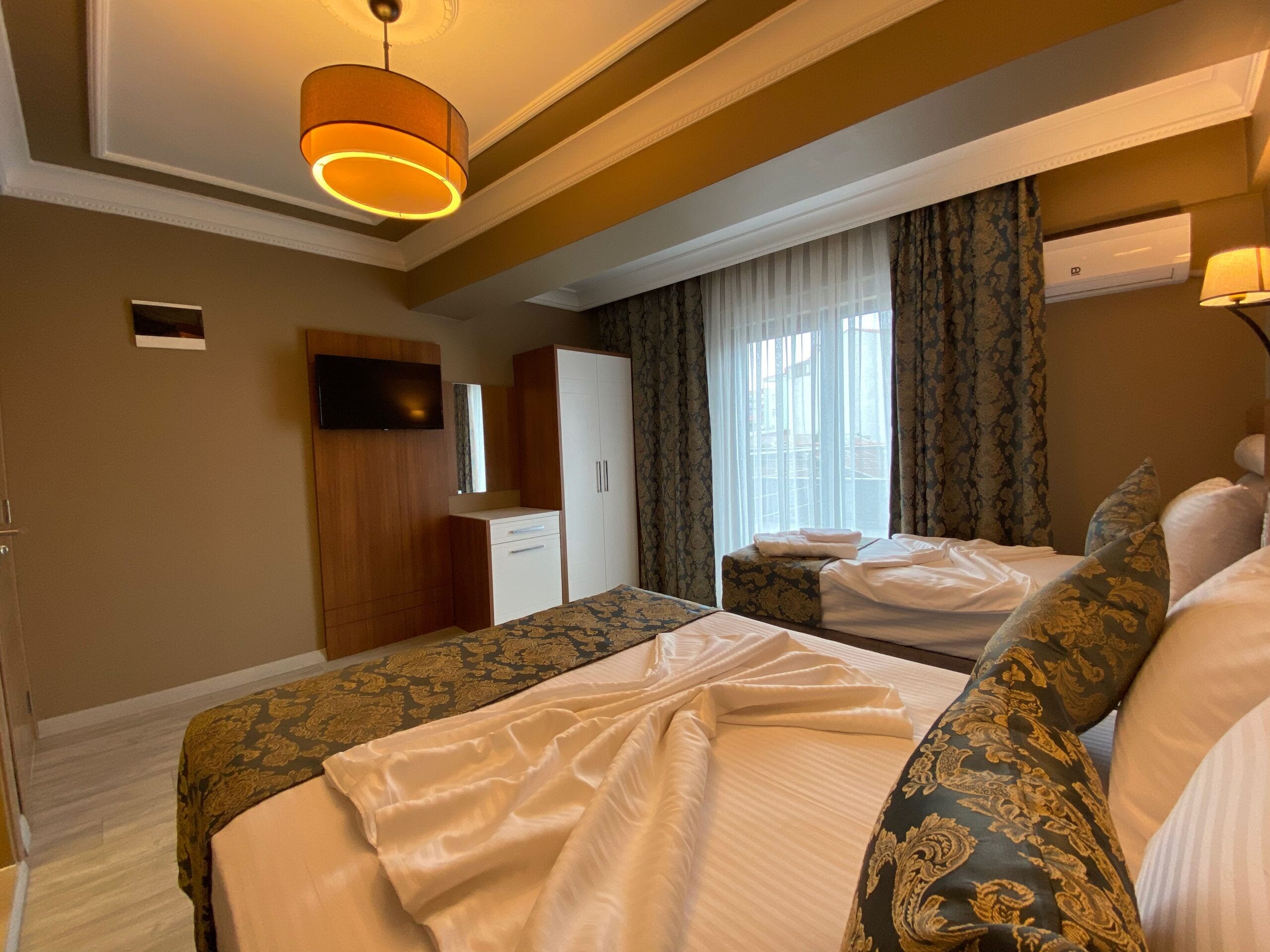 A hotel room with a bed, a desk, a mirror, a television, and a window with curtains.