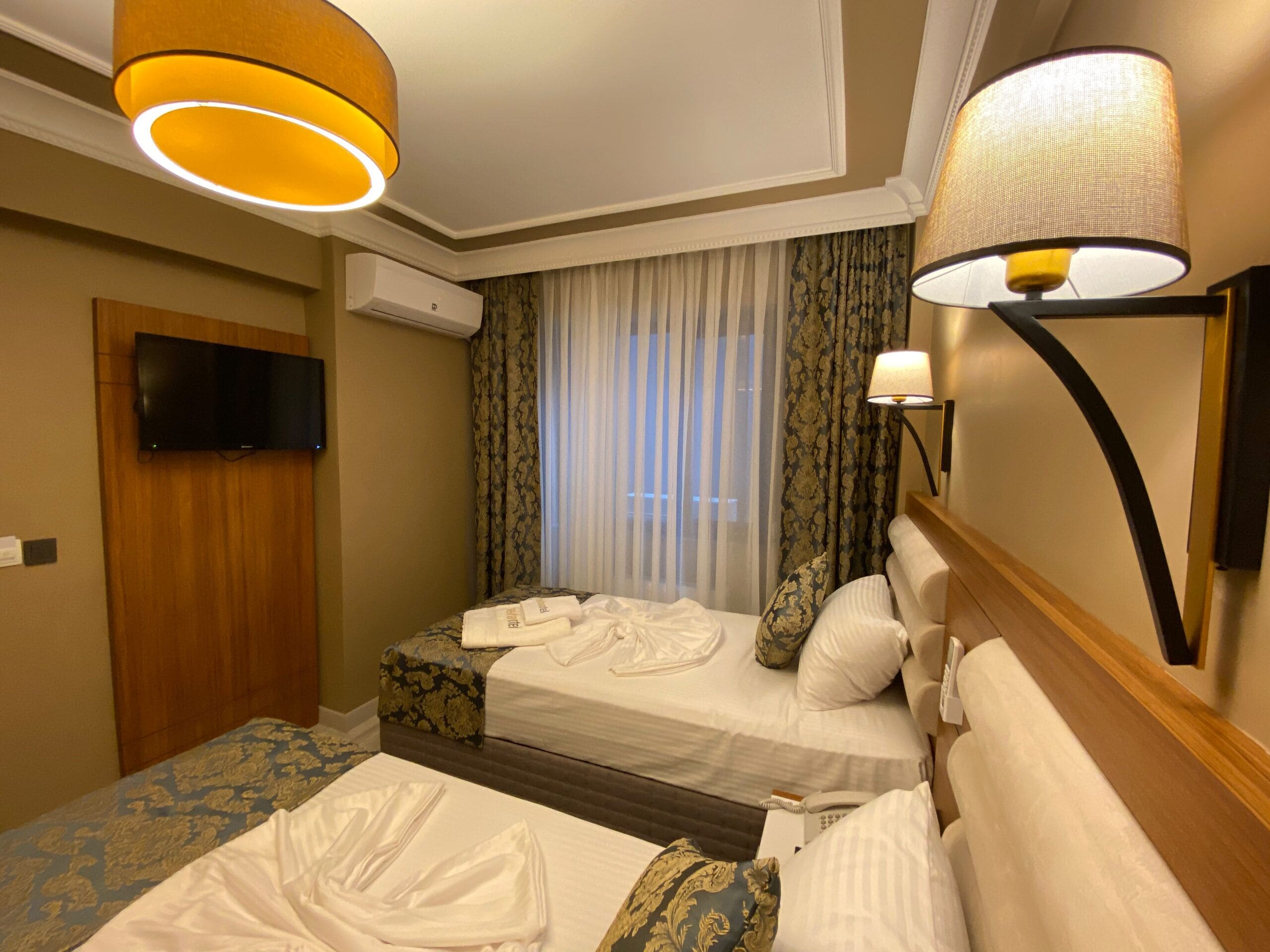 Ein Hotelzimmer mit zwei Betten, einem Fernseher, einer Klimaanlage und einer Lampe.