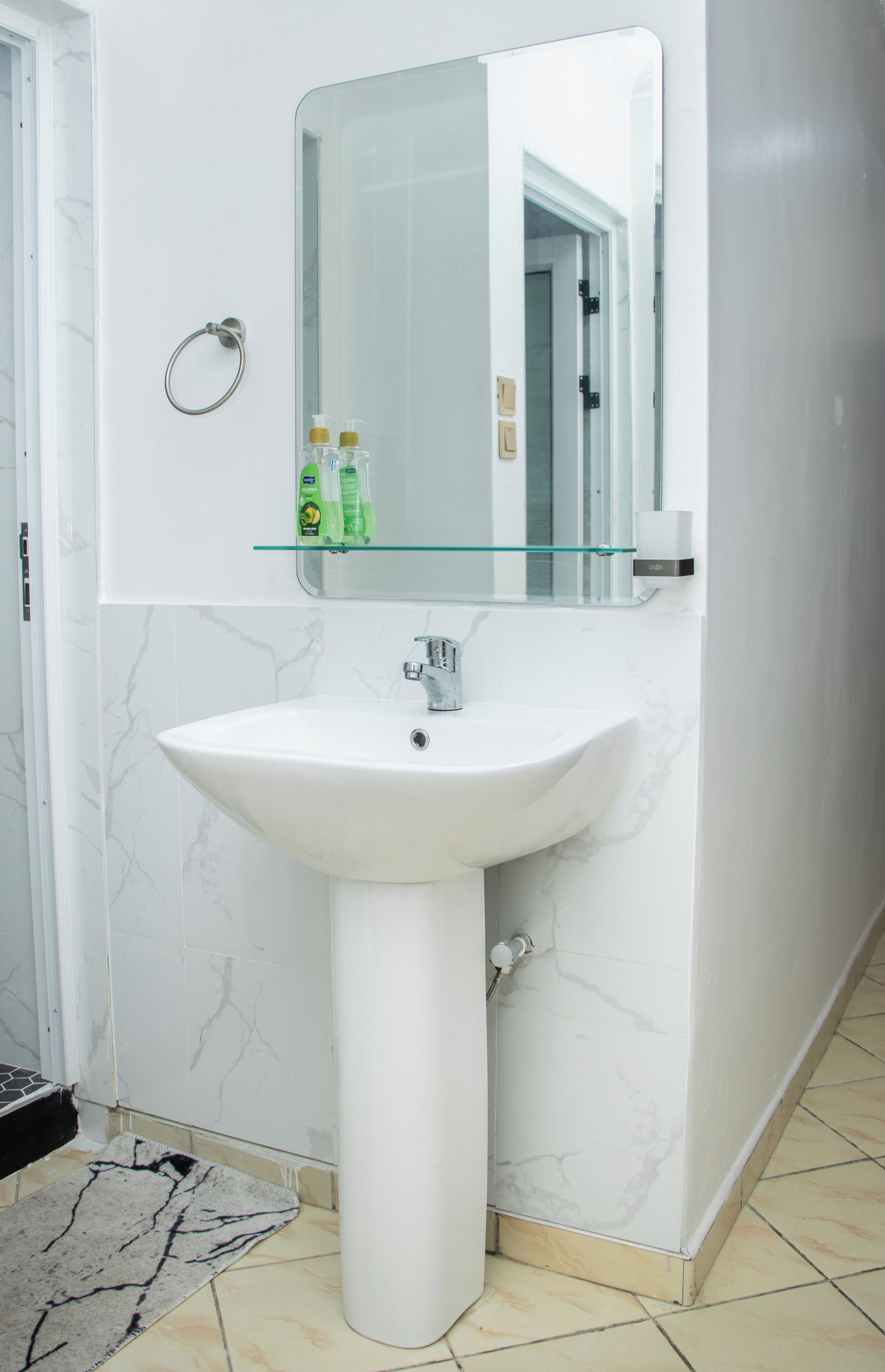 Une salle de bain avec un lavabo blanc, une étagère en verre où sont rangés les articles de toilette et un miroir.