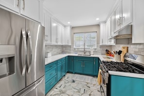 A modern kitchen with stainless steel appliances, teal cabinetry, and a patterned floor. - Great home on the South end of St Simons (Saint Simons Island)