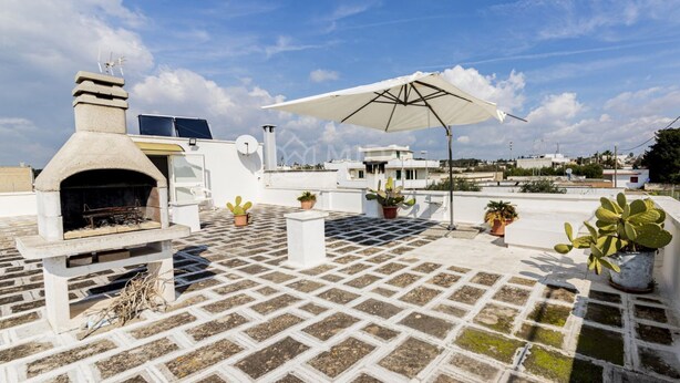 Eine Dachterrasse mit Steinofen, Kübelpflanzen und einem weißen Sonnenschirm.