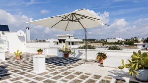 Eine Dachterrasse mit Topfpflanzen, einem weißen Sonnenschirm und blauem Himmel.