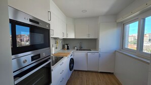 Ett modernt kök med vitvaror i rostfritt stål, en inbyggd ugn, en tvättmaskin och ett fönster med utsikt över staden.
