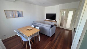 Ett modernt vardagsrum med ett matbord, en grå soffa och en platt-TV som är monterad på väggen.