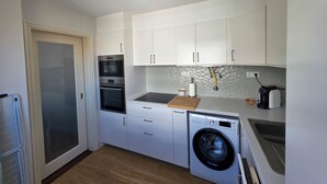 Ett kompakt kök med vita skåp, en inbyggd ugn, en mikrovågsugn, en tvättmaskin och ett handfat.