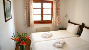 Een hotelkamer met twee bedden, een raam met bloemen gordijnen, een lijst met een afbeelding aan de muur, en een vaas met bloemen.