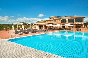 Una piscina con lettini, una zona relax coperta e un edificio con ampie finestre e pannelli solari.