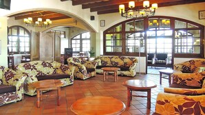 Een ruime lobby met hoge plafonds, grote ramen en diverse zithoeken, waaronder banken en tafels.
