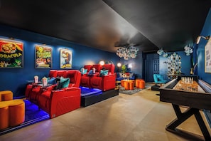 A room with a red sofa, a foosball table, and movie posters on the wall. - Heated Indoor Pool ~ Spa ~ Movie Theather ~ Gym/Yoga ~ Arcade ~ Bowling ~Karaoke (Williamston)