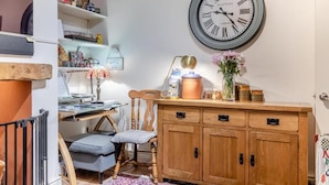 Et værelse med et træskab, et vægur, et skrivebord med en lampe og en stol.