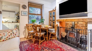 En hyggelig stue med pejs, et spiseområde med træstole, og et køkken i baggrunden.