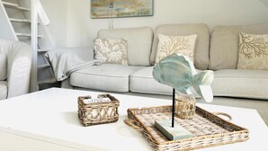 A living room with a sofa, a painting, wicker baskets, and a glass on a table. - Idyllic Thatched Apartment, Schwalbe Wieck Darß, 2 Bedrooms, 2 Balconies, Near Water (Wieck auf Darß)