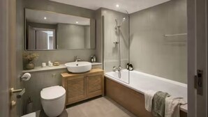 A modern bathroom with a toilet, sink, mirror, shower, and bathtub. - Prime Shoreditch – 2 Bed Central Apartment (London)