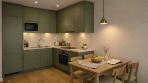 A modern kitchen with green cabinets, a microwave, a sink, and a dining area with a table and chairs. - Prime Shoreditch – 2 Bed Central Apartment (London)