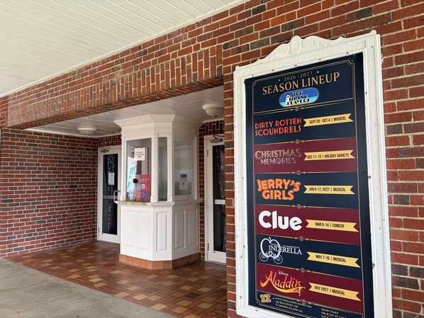 A brick building entrance with a ticket booth and a season lineup poster listing shows like Dirty Rotten Scoundrels and Clue. - Spacious 4 Bed/3 Bath house with pool, fenced backyard, fire pit, covered porch. (St. Simons Island)