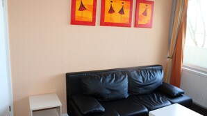 A black leather sofa with cushions, a white side table, and three framed artworks on the wall. - Holiday apartment on the Baltic Sea E312 (Schönberg OT Holm)