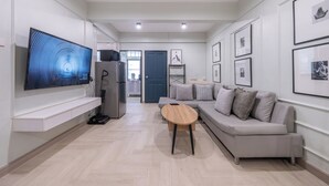 A modern living room with a flat-screen TV, a wooden coffee table, a grey sofa, and framed artwork on the walls. - Arun Sa Wad House Lad phrao 4 Guests (Bangkok)