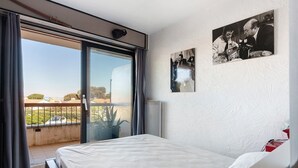 Une chambre à coucher avec un lit, une porte-fenêtre coulissante donnant sur un balcon et deux tableaux encadrés accrochés au mur.