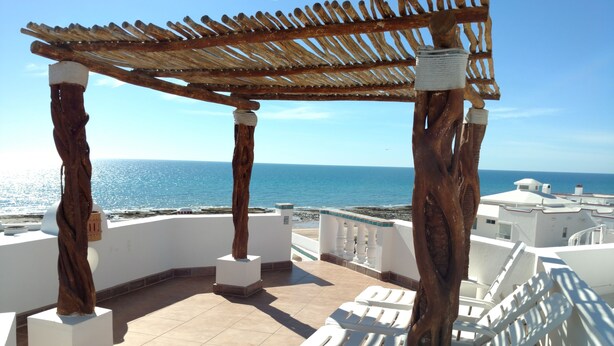 Een terras met witte loungestoelen, een houten pergola en uitzicht op zee.