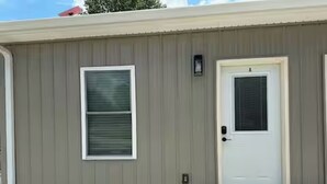 A building with a white door, a window with blinds, and a small porch.