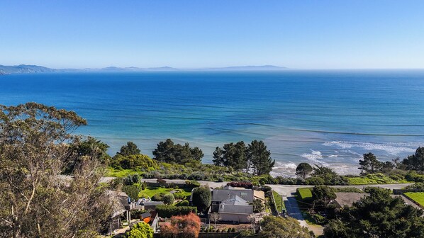 A coastal residential area with houses, a clear view of the ocean, and distant mountains.