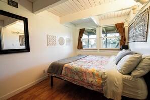 A bedroom with a bed, a window with curtains, a mirror, and wall decorations.