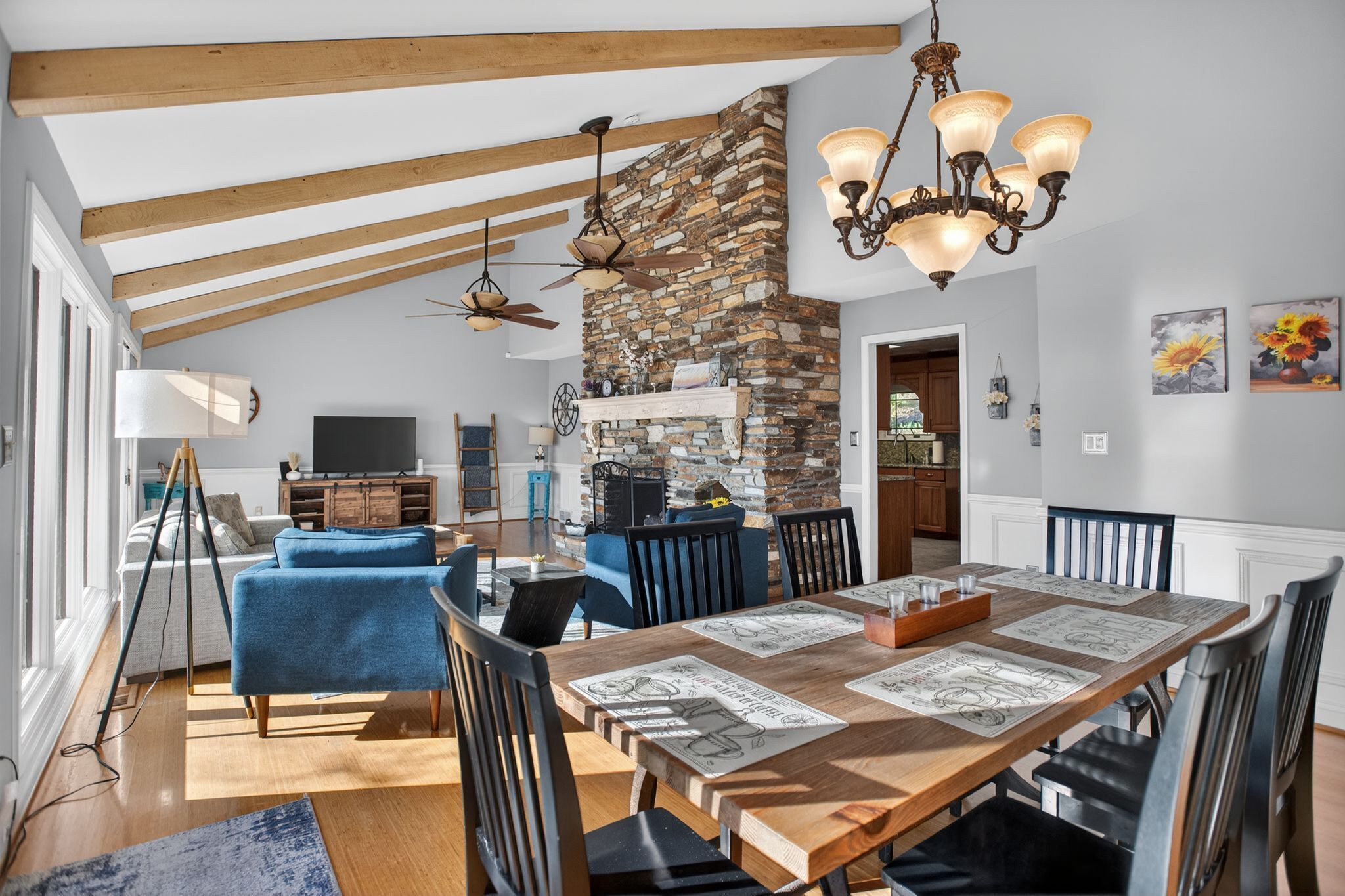 A spacious living area with a high ceiling, exposed beams, a stone fireplace, and a dining table set for six.