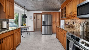 Una cocina con armarios de madera, un refrigerador de acero inoxidable, encimeras de granito y una estufa moderna.
