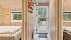 Una cabaña de madera con una puerta central, dos ventanas a cada lado y un piso de baldosas.
