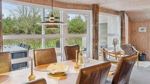 Un comedor con una mesa dispuesta para cuatro, ventanas amplias y techo de madera.