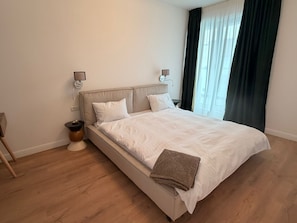 A bedroom with a bed, bedside tables, a lamp, and a window with curtains.
