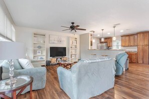A living room with a TV, sofa, and coffee table, a kitchen with wooden cabinets, and a ceiling fan. - Coastal Getaway: Near FIT, Downtown & Beach (Melbourne)