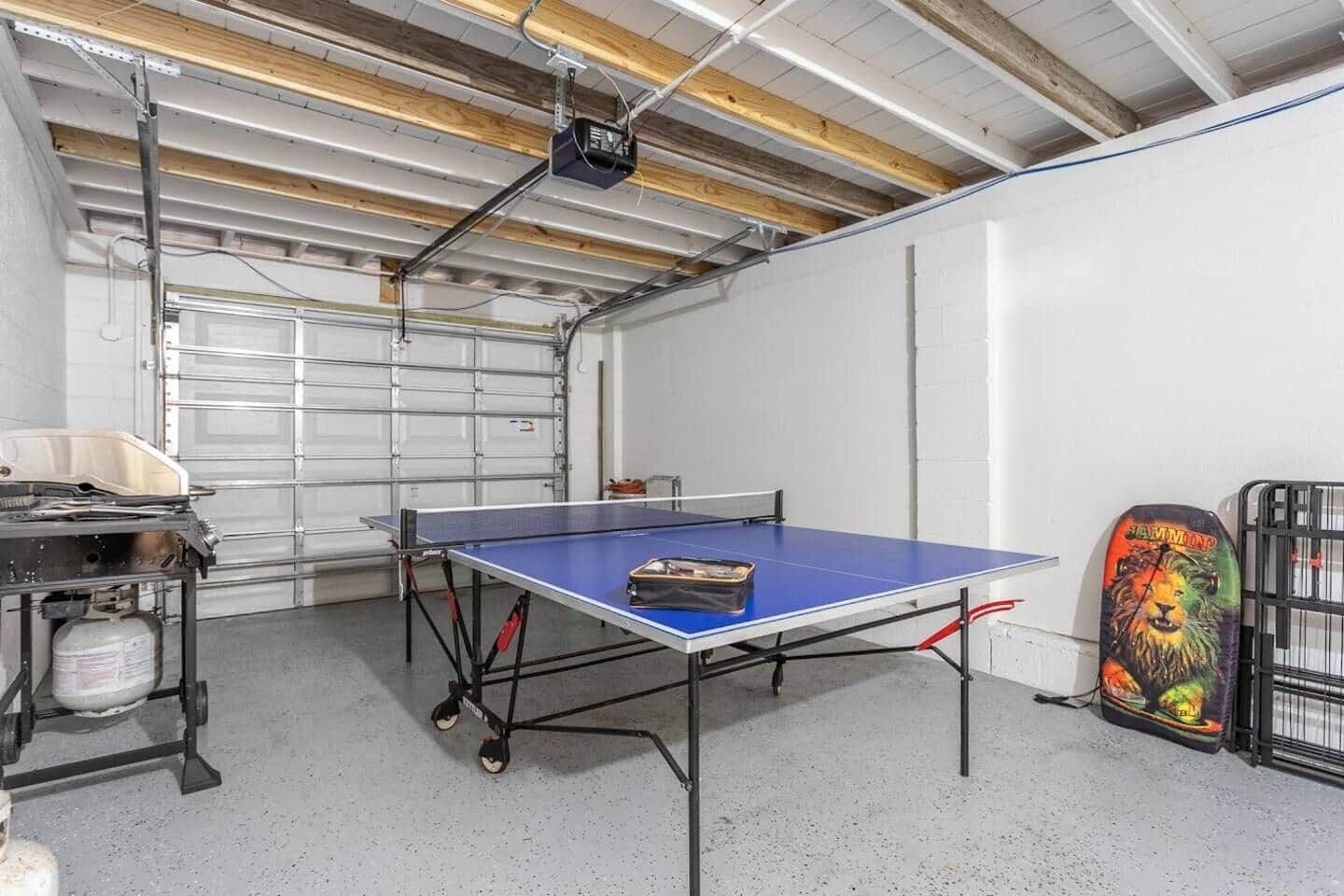 A ping pong table in a room with a garage door, a gas cylinder, and a colorful helmet on the wall.