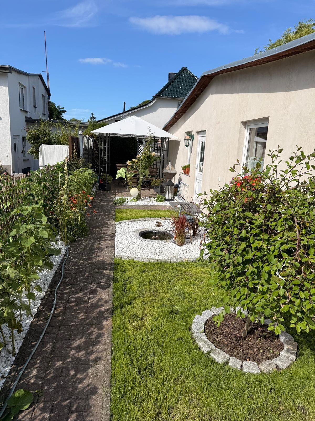 A garden pathway leading to a covered patio area with a small pond and potted plants.