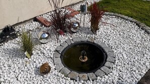 Ein Garten mit Wasserspiel, Kieselsteinen und Pflanzen.
