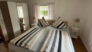 Ein Schlafzimmer mit Bett, Nachttischen, einem Kleiderschrank, einem Fenster mit Vorhängen und einer Deckenleuchte.