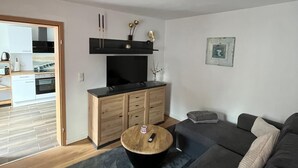 Ein modernes Wohnzimmer mit einem grauen Sofa, einem Holztisch und einem Fernseher auf einer Holzkommode.
