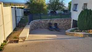 Un patio con un muro de piedra, un pequeño jardín y un árbol alto.