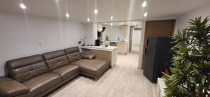 Ein modernes Wohnzimmer mit einer braunen Ledersofa, einer Küchenzeile mit weißer Arbeitsplatte und einem schwarzen Kühlschrank.