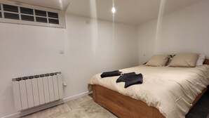Un dormitorio con cama de madera, ropa de cama color crema, una mesita de noche, un radiador y una ventana con persianas.