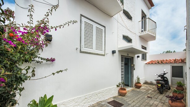 A courtyard with a white building, potted plants, a scooter, and a door. - Cantinho da Lurdes in Cabanas de Tavira (Tavira)