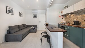 A modern kitchen with a built-in stove, a dining area with a bar counter, and a grey sofa in a compact living space. - Cantinho da Lurdes in Cabanas de Tavira (Tavira)