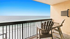 Un balcon avec vue sur la plage, une chaise en bois et un sol à motifs.