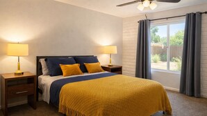 Um quarto com uma cama, duas mesas de cabeceira, um ventilador de teto e uma janela com cortinas.