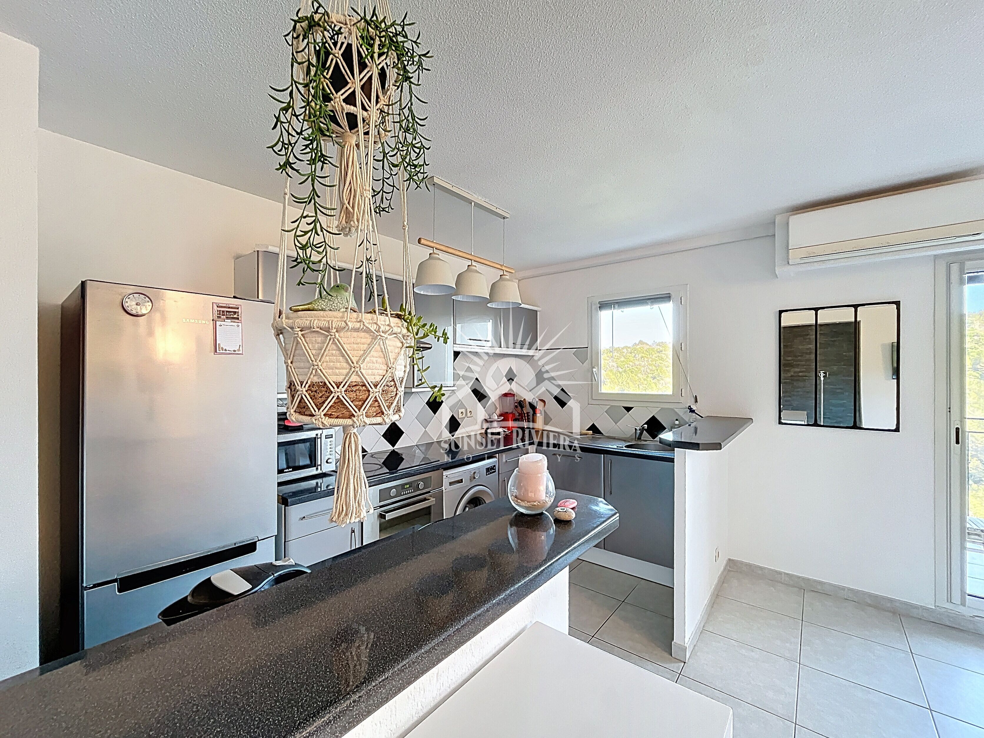 Una cocina moderna con un refrigerador de acero inoxidable, una encimera negra y una planta de macramé colgante.