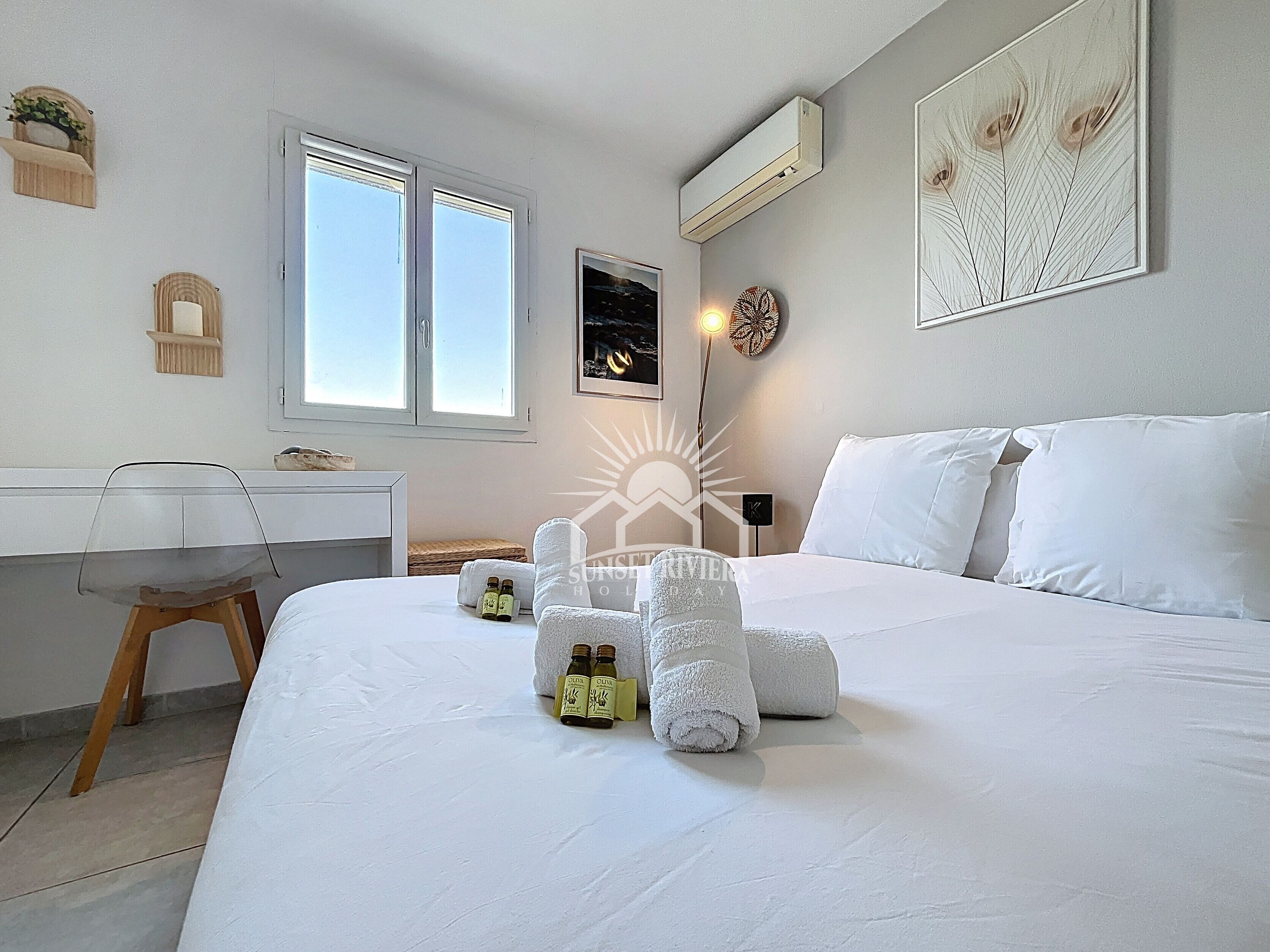 Habitación de hotel con cama, escritorio, silla, ventana, aire acondicionado y decoración en la pared.