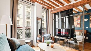 Un salon moderne doté d’un grand téléviseur, d’un canapé, d’une table basse et de grandes fenêtres offrant une vue sur les bâtiments.