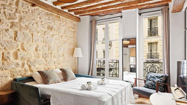 Une pièce avec un mur en pierre, un lit avec du linge de maison blanc, un canapé bleu, une chaise et un téléviseur.